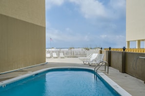 A swimming pool with lounge chairs and a view of the beach.
