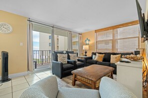 A living room with a sofa set, a coffee table, a TV, and a window with blinds.