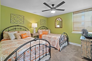 A bedroom with two beds, a ceiling fan, a bedside table with a lamp, a window with blinds, and a decorative mirror. - GULF HOUSE #103, GREAT LOCATION, BEACH FRONT, 1ST FLOOR (Gulf Shores)