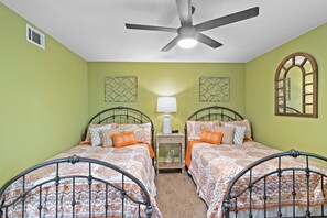 A bedroom with two beds, a ceiling fan, a nightstand, and decorative wall art.