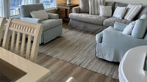 Una sala de estar con vista al océano, un ventilador de techo, un cuadro de la playa y una lámpara.