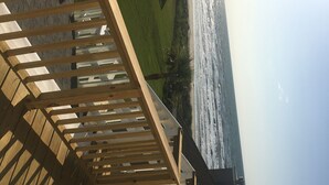 A wooden staircase leading to a covered area with a view of a grassy landscape. - Almost Beachfront- Beautiful Pirates Beach home- Sleeps 14-Steps to beach!! (Galveston)