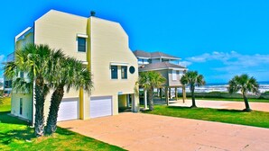 A two-story residential building with a garage, palm trees, and a clear view of the ocean. - Almost Beachfront- Beautiful Pirates Beach home- Sleeps 14-Steps to beach!! (Galveston)