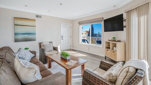 A modern living room with a sofa, coffee table, and wicker chairs. A flat-screen TV is mounted on the wall, and there is a window with a view of buildings. - Oceanfront with incredible views.
Last minute discounts Available (San Diego)