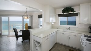 A modern kitchen with white cabinetry, a dining area with a view of the ocean, and a large window with a view of the sea. - Oceanfront with incredible views.
Last minute discounts Available (San Diego)