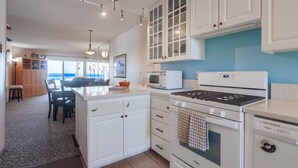 A modern kitchen with white cabinetry, a microwave, a stove, and a dishwasher. There is a dining area with a table and chairs visible in the background. - Awesome ocean front condo in the heart of Mission Beach! (San Diego)