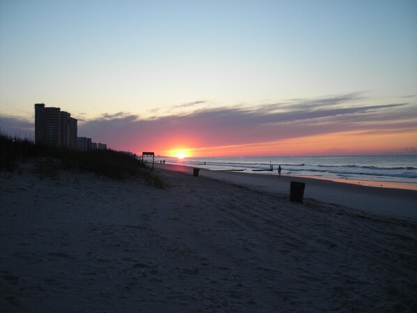 A beach with a sunset, a high-rise building, and a few people walking. - DIRECT OCEANFRONT, 1ST FLOOR, SPECTACULAR VIEWS!! DISCOUNTS AVAILABLE (North Myrtle Beach)