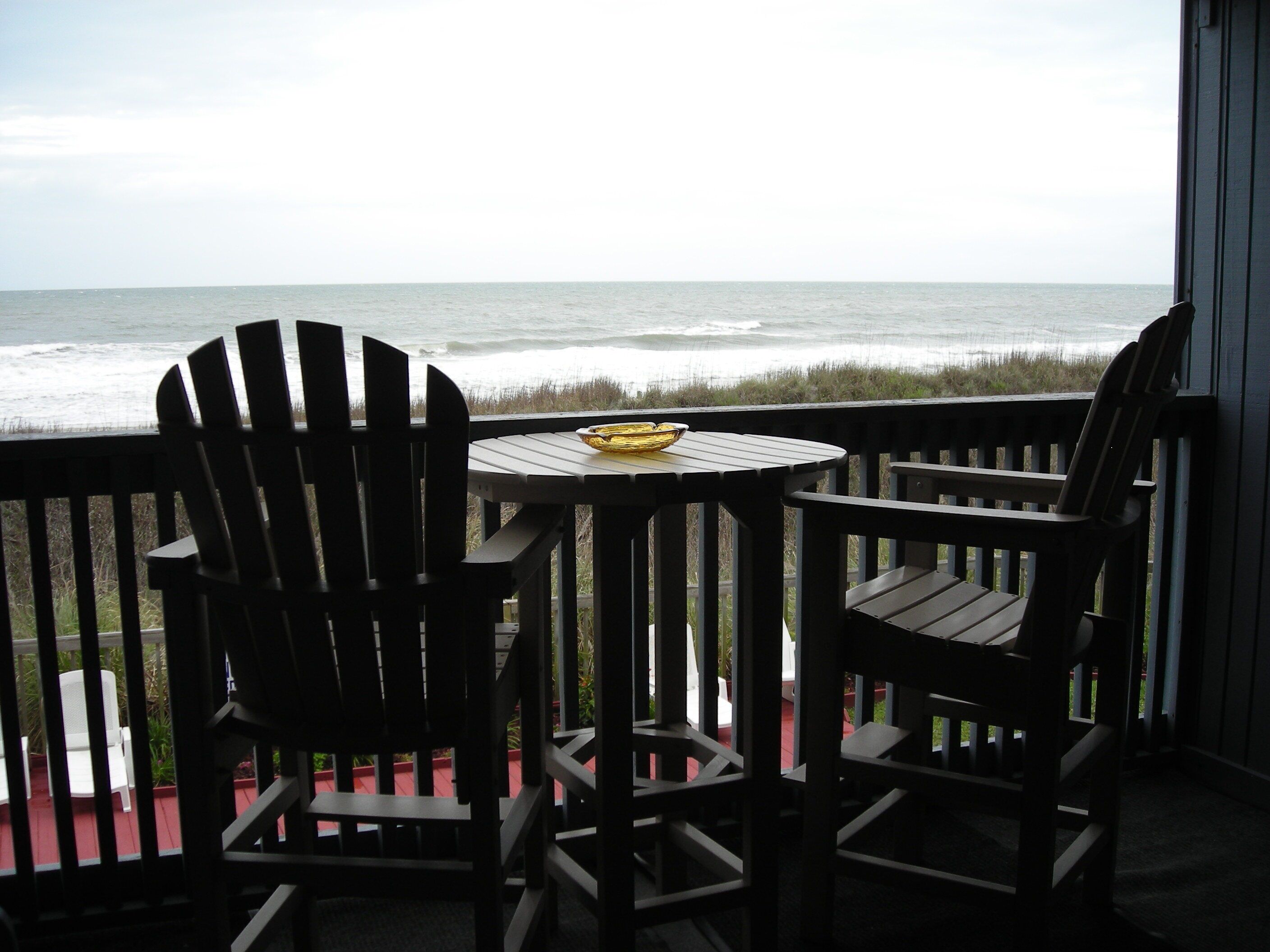 Een terras met twee Adirondack-stoelen en een kleine tafel, met uitzicht op de oceaan.