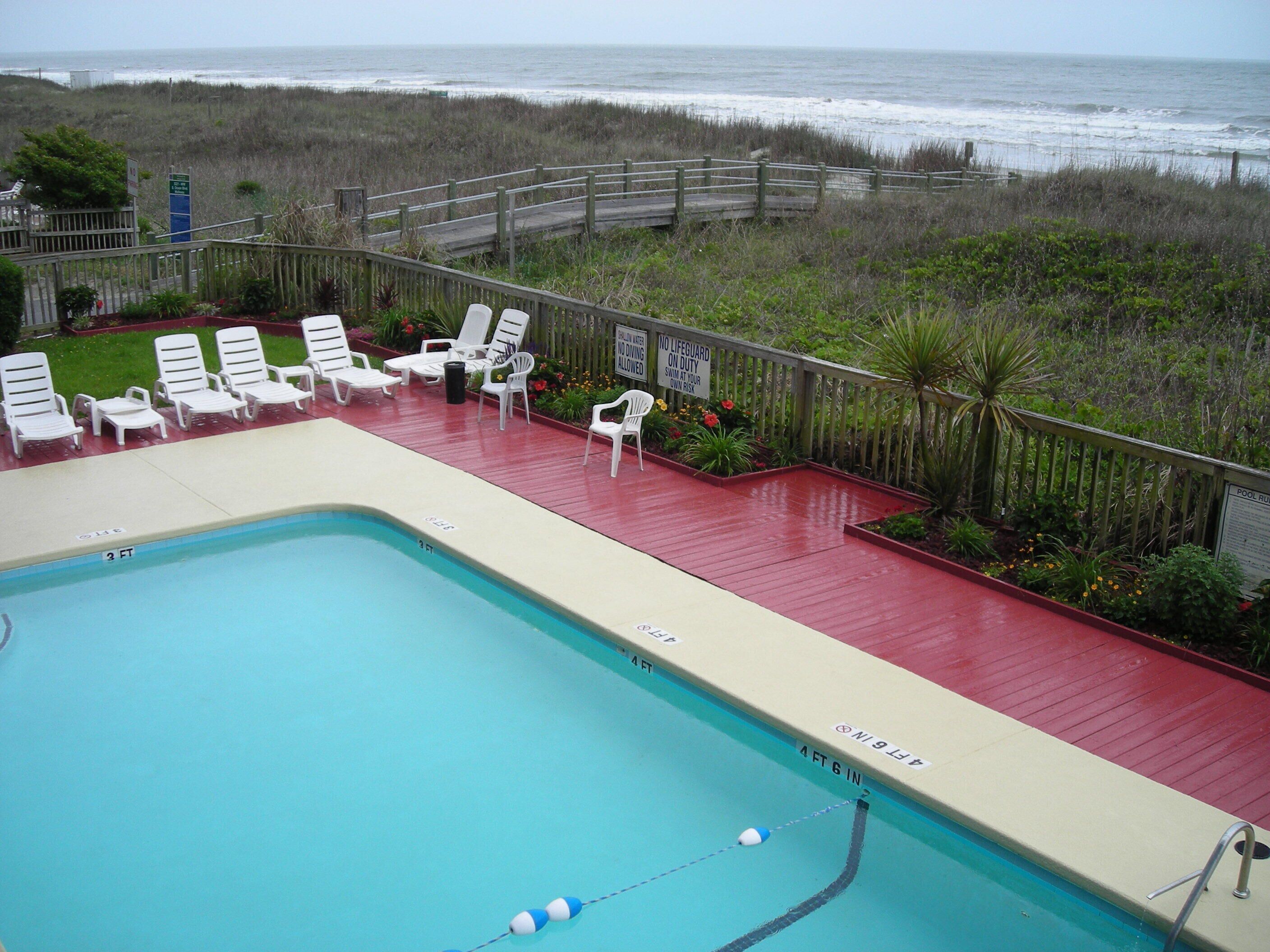 A swimming pool with lounge chairs and a wooden deck overlooking the ocean.