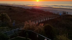 Ein Sonnenuntergangsblick von einer Strandlage mit einer Holzpromenade und grasbewachsenen Dünen.
