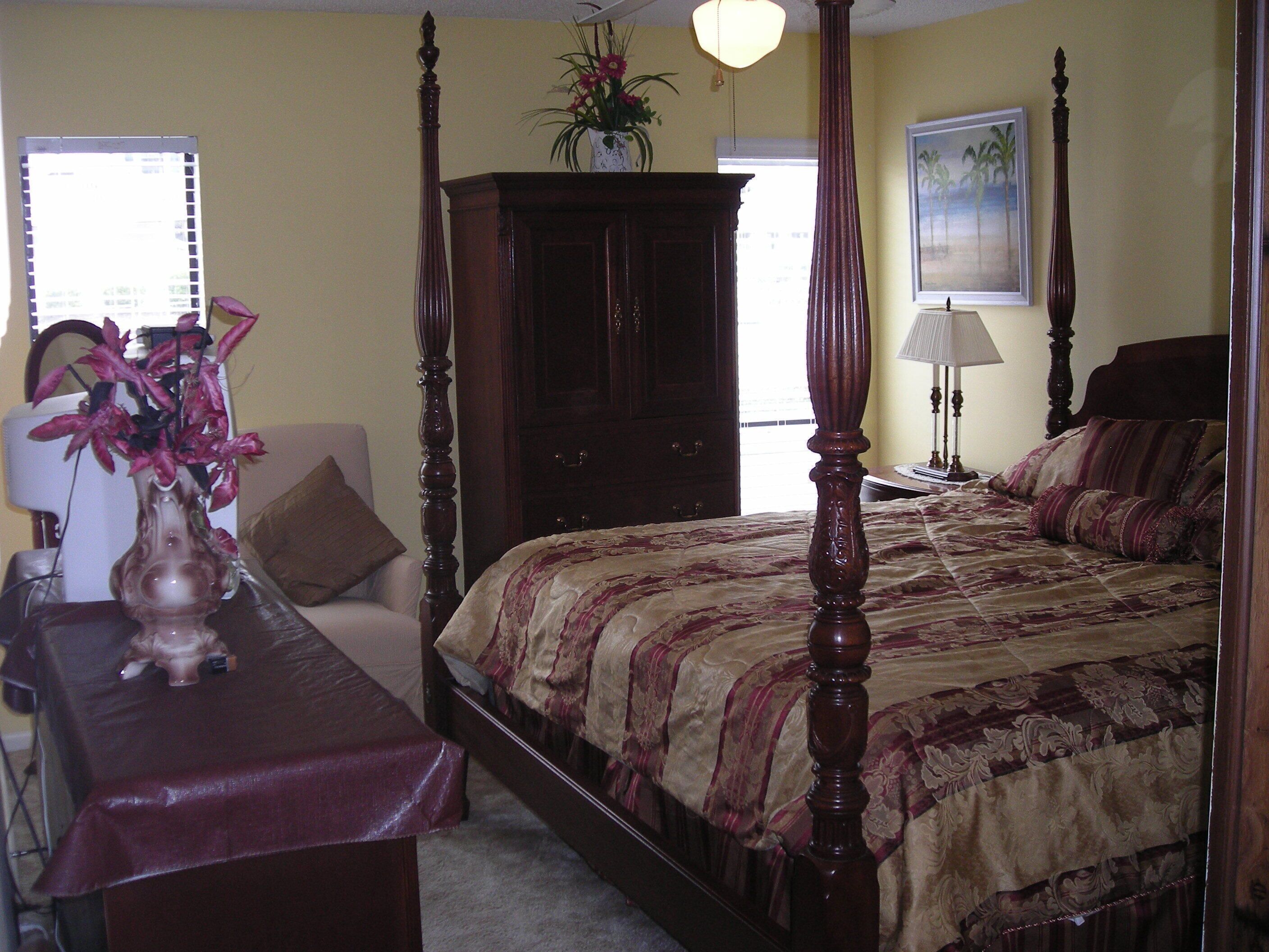 A bedroom with a four-poster bed, a nightstand, a desk, and a chair.