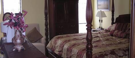 A bedroom with a four-poster bed, a nightstand, a desk, and a chair.