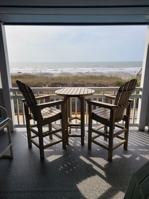 A balcony with two wooden chairs and a small table, overlooking a beach with waves and people in the distance. - DIRECT OCEANFRONT, 1ST FLOOR, SPECTACULAR VIEWS!! DISCOUNTS AVAILABLE (North Myrtle Beach)