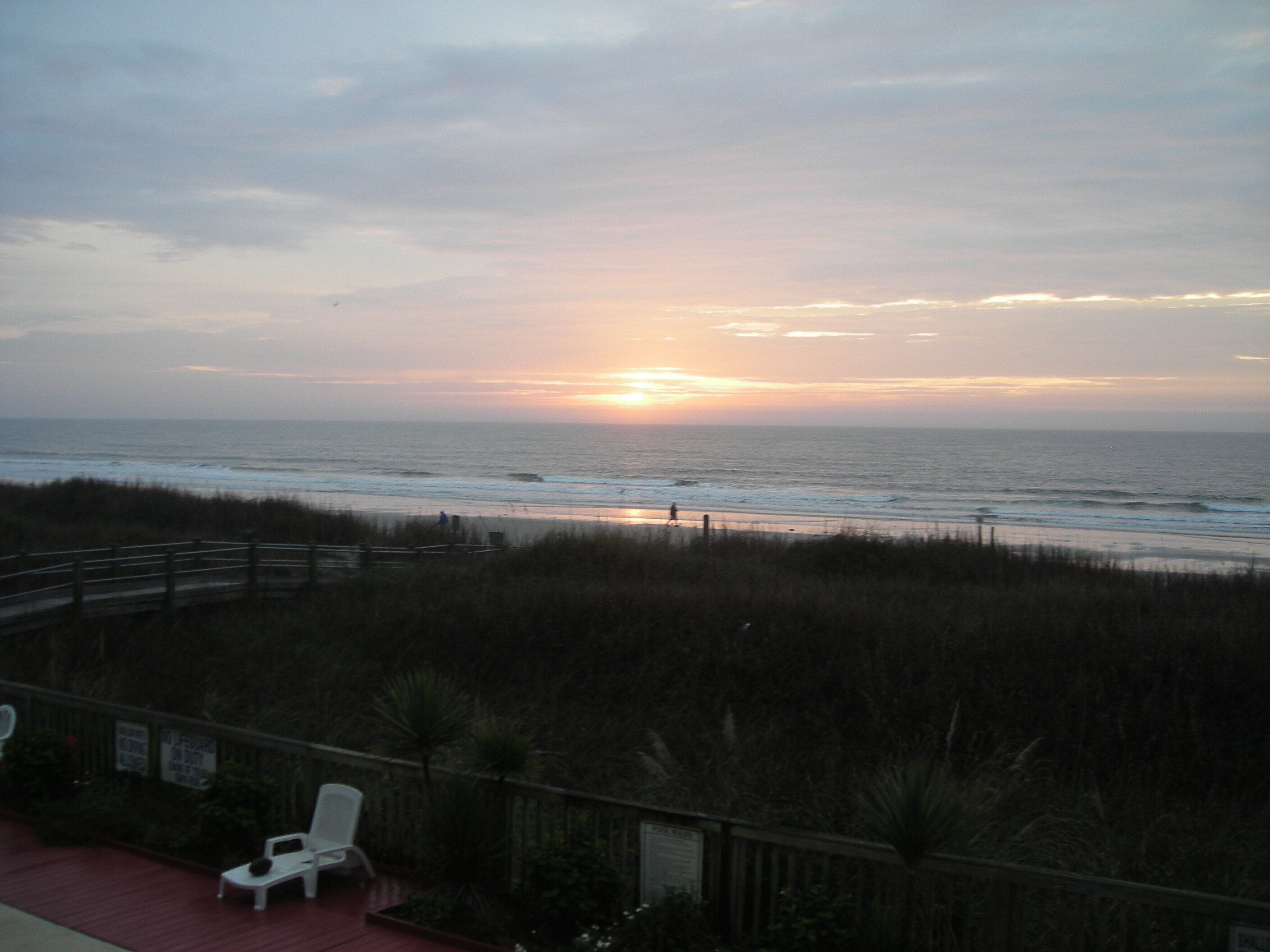 A beach view with a wooden deck and a white chair.