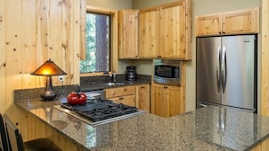 Una cucina con mobili in legno, piani di lavoro in granito, frigorifero in acciaio inossidabile, forno a microonde, piano cottura e bollitore.