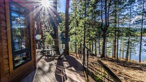 Un terrazzo in legno con tavolo e sedie, affacciato su una foresta e un lago.