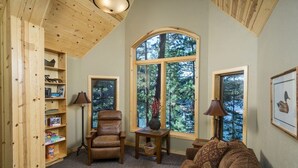 Una stanza accogliente con soffitto in legno, una poltrona in pelle, un divano marrone e un'ampia finestra con vista sugli alberi.