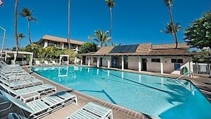 A swimming pool with lounge chairs, palm trees, and a building with solar panels. - Stay in Kihei - Newly Updated - Three Minute Walk to Kamaole II Beach! (Kihei)
