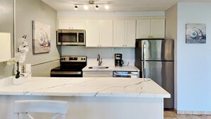 A modern kitchen with white cabinets, a stainless steel refrigerator, a microwave, and a coffee maker. - Stay in Kihei - Newly Updated - Three Minute Walk to Kamaole II Beach! (Kihei)