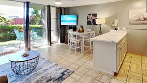 A modern kitchen with a central island, a dining area with white chairs, and a TV mounted on the wall. - Stay in Kihei - Newly Updated - Three Minute Walk to Kamaole II Beach! (Kihei)