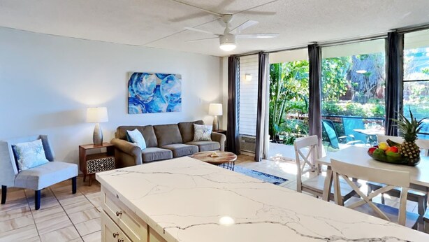 A modern kitchen with a marble island, a dining area with a table and chairs, a sofa, and a ceiling fan. - Stay in Kihei - Newly Updated - Three Minute Walk to Kamaole II Beach! (Kihei)