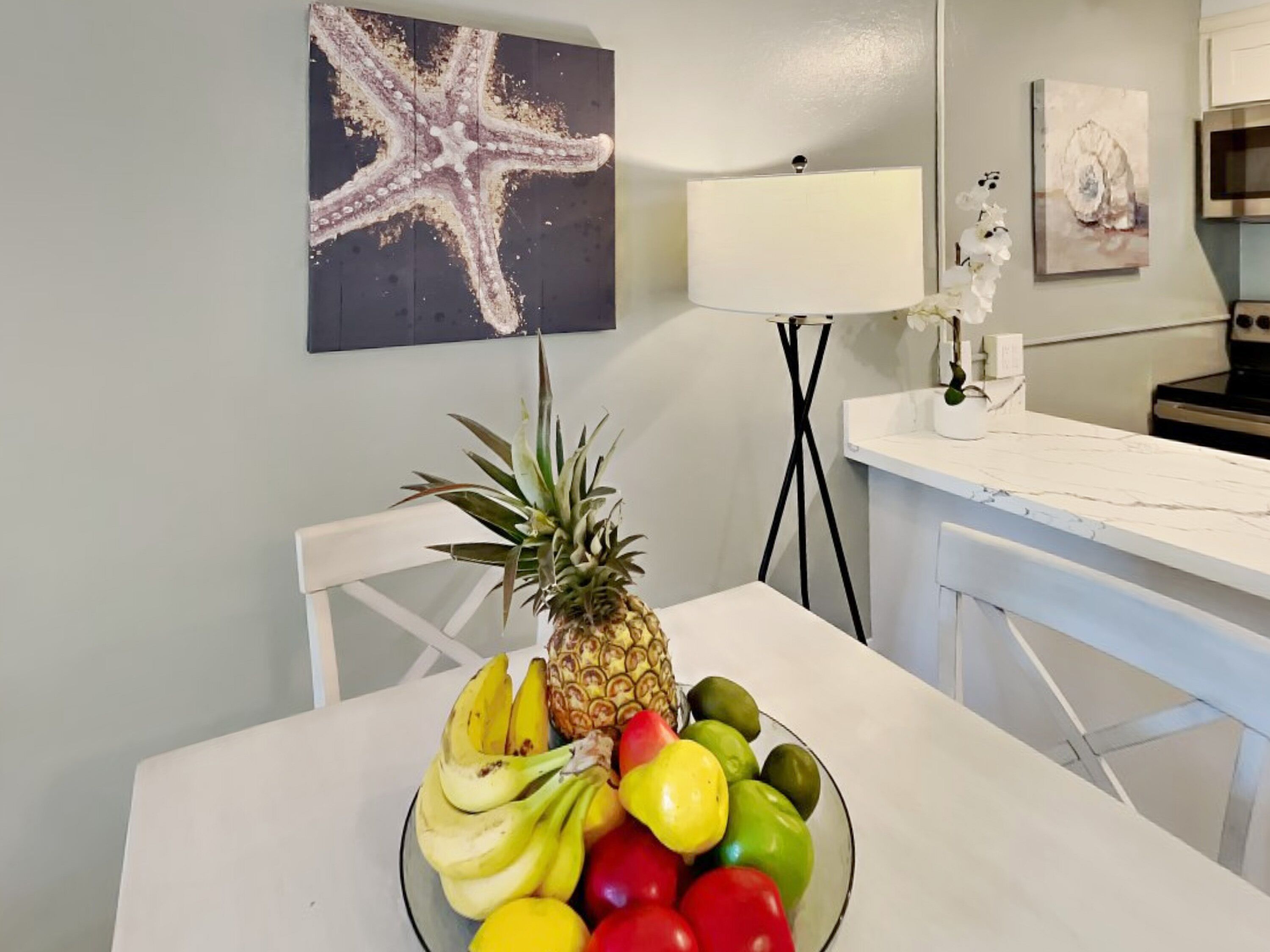 A dining area with a table set for a meal, featuring a bowl of fruit and a pineapple centerpiece.