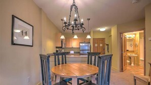 A dining area with a wooden table and chairs, a chandelier, and a kitchen in the background. - SM8175, Heart of River Run Village! (Keystone)