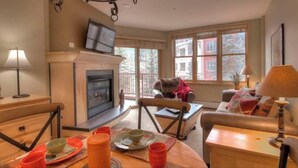 A cozy living room with a fireplace, a dining table set with plates and cups, and a comfortable seating area with a sofa and armchairs. - SM8175, Heart of River Run Village! (Keystone)