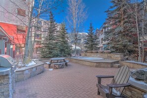An outdoor patio area with brick flooring, picnic tables, and a barbecue grill.