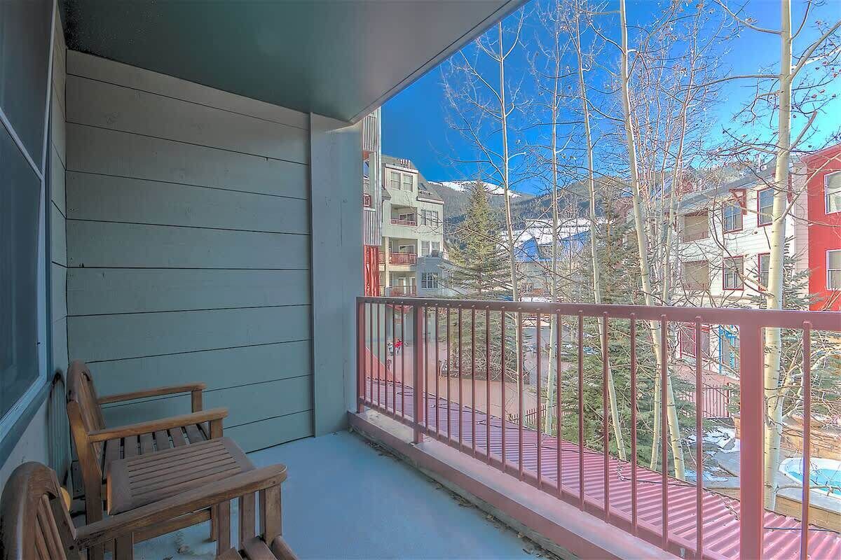 A balcony with a wooden chair, a metal railing, and a view of neighboring buildings and trees.