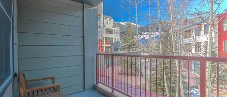 A balcony with a wooden chair, a metal railing, and a view of neighboring buildings and trees.