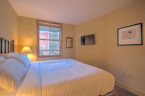Un dormitorio con una cama grande, una ventana con persianas, un televisor y cuadros en la pared.
