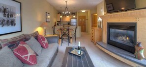 Una sala de estar acogedora con chimenea, un comedor y una cocina al fondo.