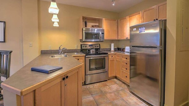 A modern kitchen with stainless steel appliances, wooden cabinets, and a built-in island with a book on it. - SM8175, Heart of River Run Village! (Keystone)