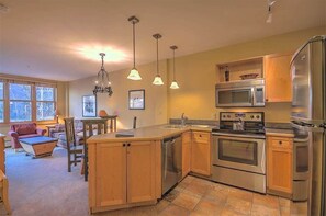Una cocina moderna con armarios de madera, electrodomésticos de acero inoxidable, iluminación colgante y un comedor con mesa y sillas.