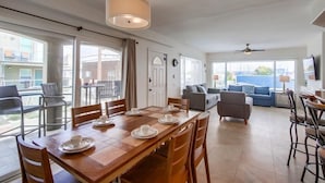 Uma sala de estar ampla com uma mesa de jantar posta para quatro pessoas, um sofá e uma TV fixada na parede.