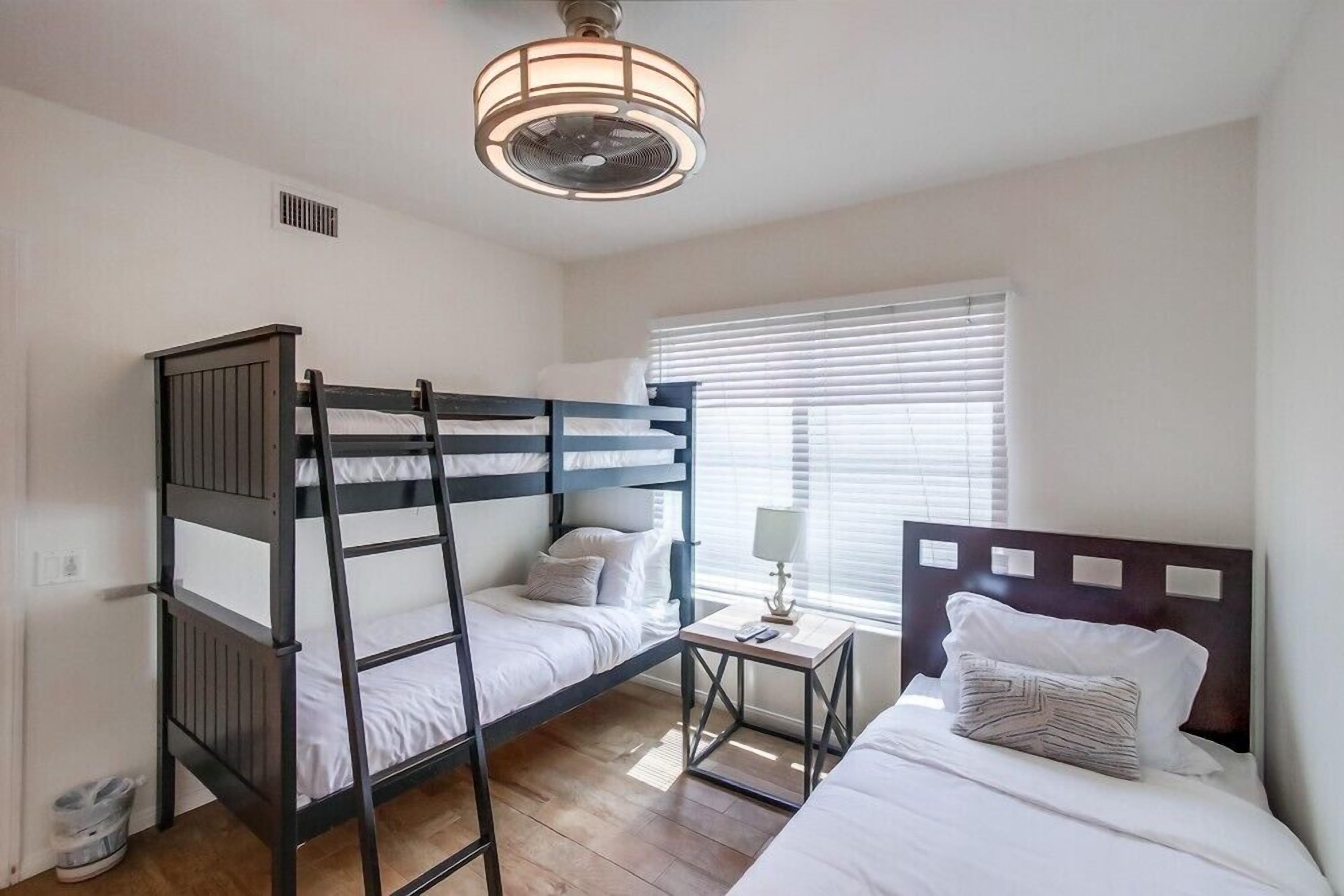 Une chambre avec un lit superposé, un lit simple, une petite table et un ventilateur de plafond.