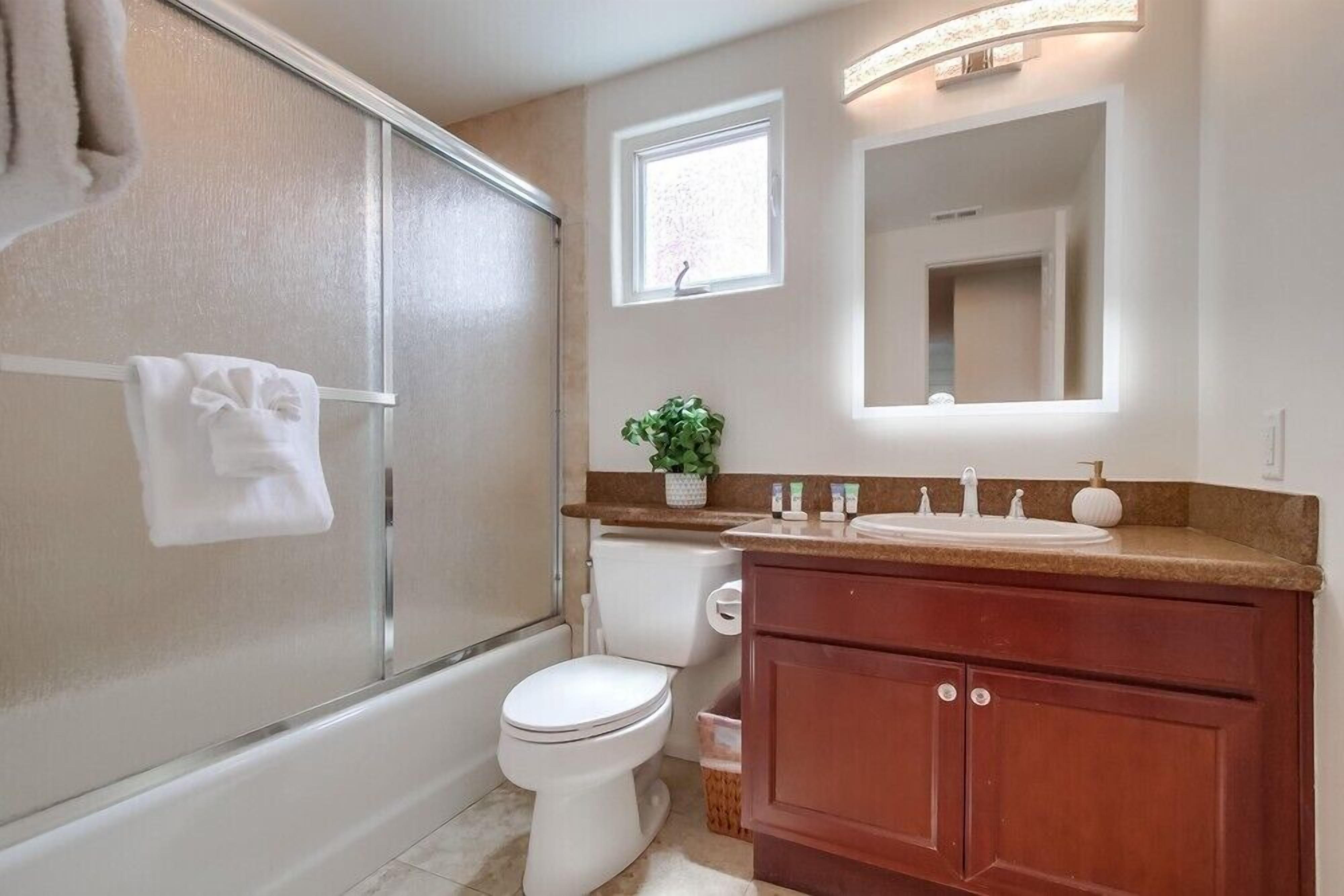 Een badkamer met een douche in een glazen cabine, een wit toilet, een wastafel met spiegel en een klein raam.