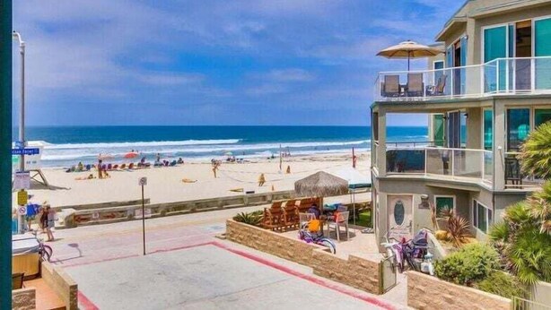 Um hotel na praia com varanda com vista para o oceano, área de pátio com mobiliário para área externa e vista da praia.