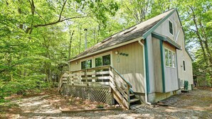 A wooden cabin with a porch, surrounded by trees. - Cozy 3 bedroom 2 bath beach house with private setting! Pool, Trolley, Wifi, Beach Town! (Bethany Beach)