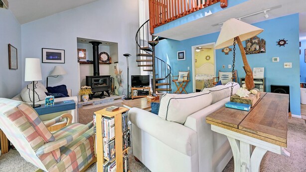 A living room with a sofa, armchair, wooden table, and a spiral staircase. - Cozy 3 bedroom 2 bath beach house with private setting! Pool, Trolley, Wifi, Beach Town! (Bethany Beach)