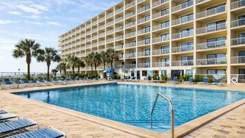 A hotel with a swimming pool, lounge chairs, and palm trees.