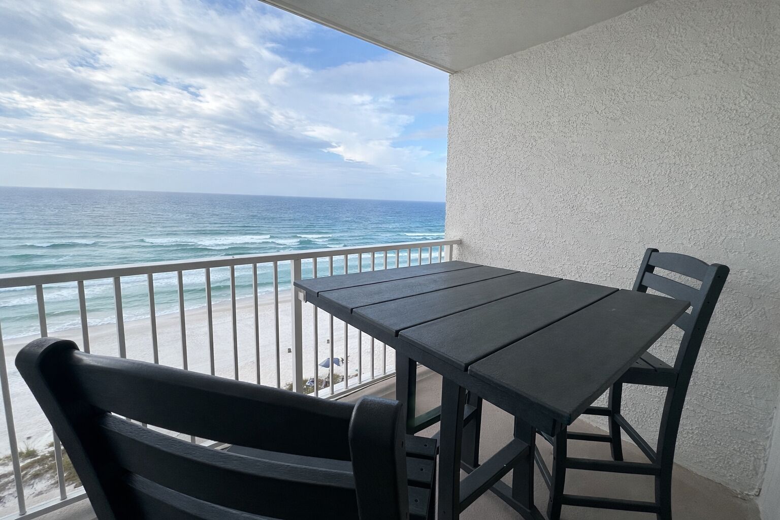 A balcony with a table and chairs overlooking a beach.