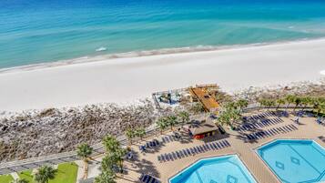 An aerial view of a beach resort with a large pool area, multiple swimming pools, and a beach with a sandy shore.
