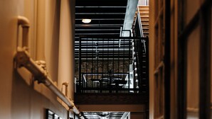 A narrow, well-lit hallway with wooden floors and a staircase leading to an upper level.
