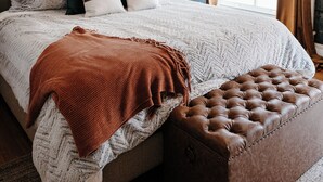 A neatly made bed with a patterned headboard, a bedside table with a lamp, and a window with curtains.