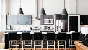 A modern kitchen with a central island, black bar stools, and pendant lighting.