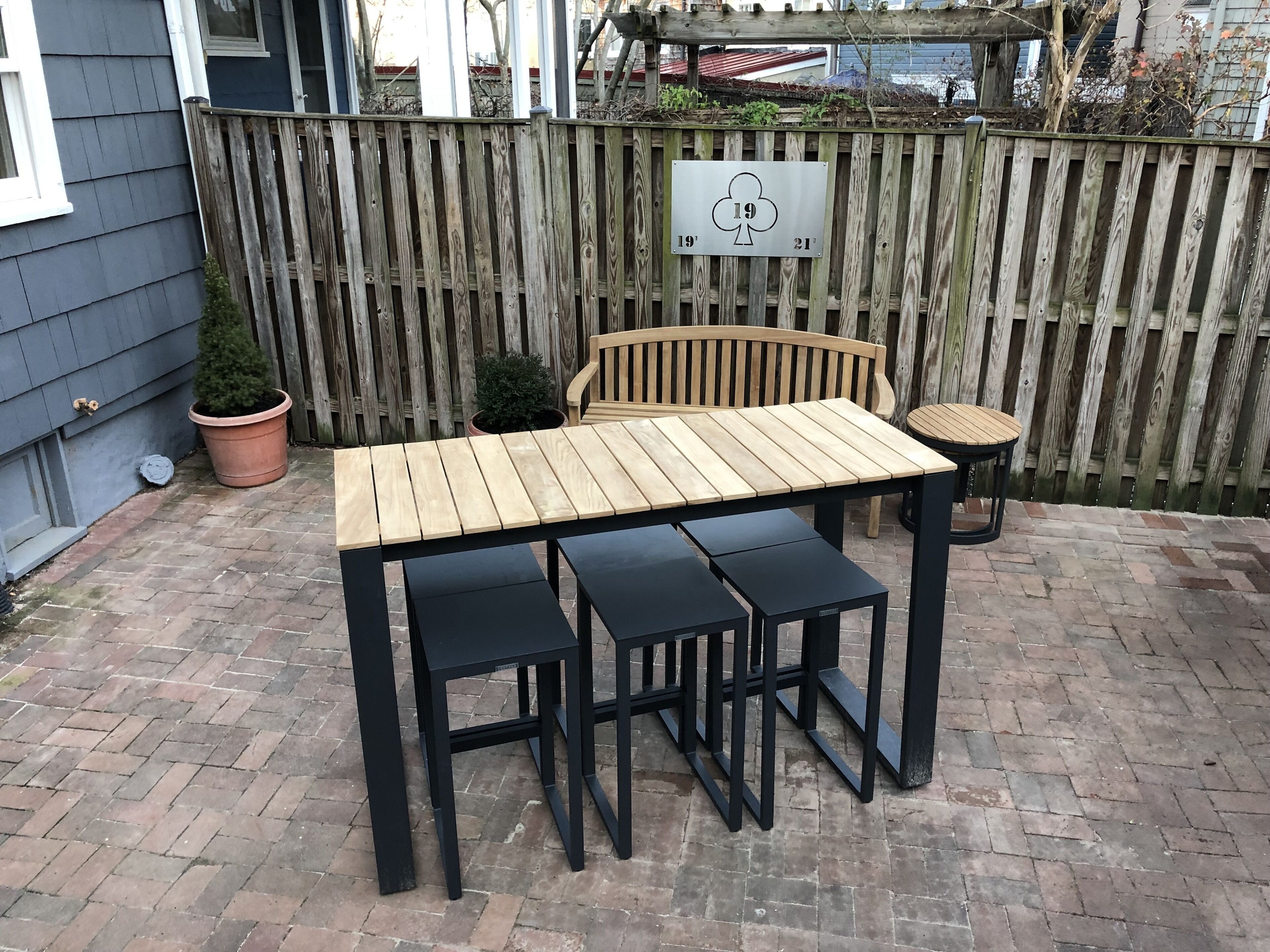Una mesa de patio de madera con cuatro sillas negras, un banco de madera y una pequeña mesa redonda.