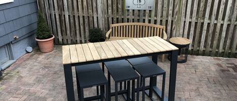 Una mesa de patio de madera con cuatro sillas negras, un banco de madera y una pequeña mesa redonda.