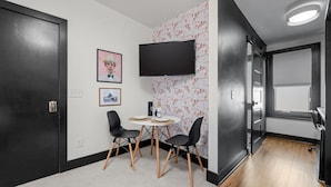 A modern room with a flat-screen TV, a small table with chairs, and a patterned wallpaper. - Heart of 12th South -  1 bed, 1 bath Cozy Suite in Nashville (Nashville)